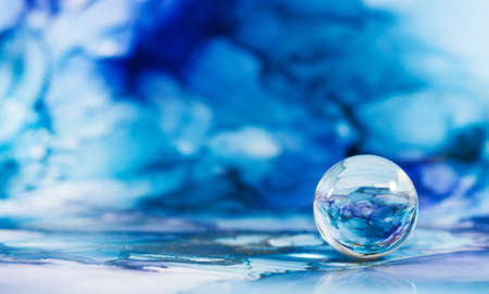 A transparent glass ball on an abstract blue background. The technique of alcoholic ink. Copy space.の写真素材