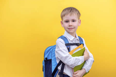 A cute boy in a shirt with a backpack on his back holding textbooks on a yellow background. Back to school.の写真素材