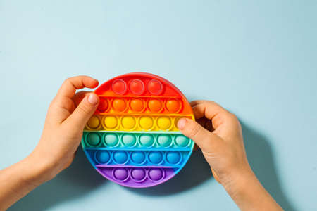 Childrens hands hold a pop it toy silicone on a blue background. Anti-stress to. Copy space.の写真素材