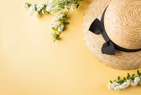 Flat lay a straw hat and a branch with white flowers on a yellow background. Summer vacation concept. Copy space.の写真素材
