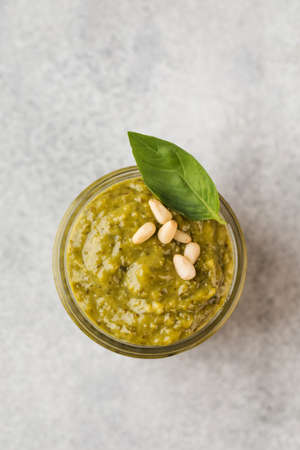 Pesto sauce in a jar with pine nuts and green basil leaves. Top view. Copy space.