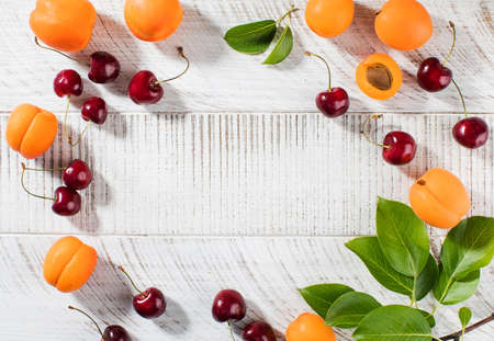 Ripe cherries and fresh apricots on a white wooden background. Summer background. Copy space.の写真素材
