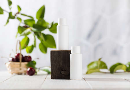 White tubes with cosmetics on a wooden podium against the background of foliage, cherry berries. Natural cosmetics.の写真素材