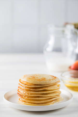 The pancakes are stacked in a plate. In the background, a bowl of honey, fruit, and a jug of milk. Copy space.の写真素材