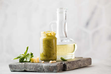 Pesto sauce with green basil leaves, slices of parmesan cheese and a jug of olive oil on a wooden board. Copy space.の写真素材