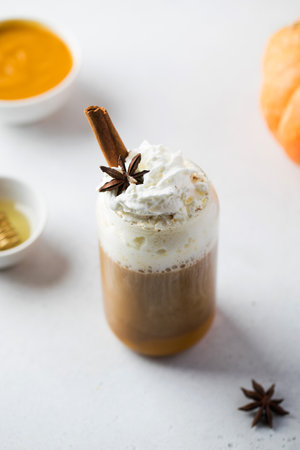 Glass of delicious sweet pumpkin coffee decorated with whipped cream cinnamon stick and anise star on light table close viewの写真素材