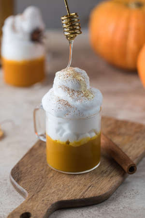 Pouring honey into pumpkin coffee in cup on wooden table