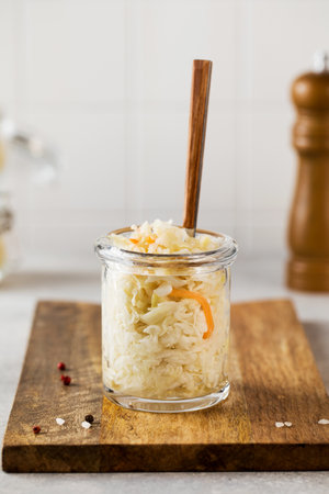 Sauerkraut in a glass jar with a fork on a wooden board. Fermentation and canning of vegetables.の写真素材