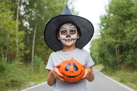 Boy with skeleton makeup and hat holds spooky pumpkinの写真素材