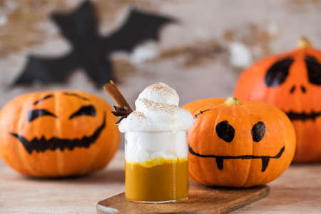 Coffee with whipped cream and scary pumpkins on wooden table. Pumpkin latte.の写真素材