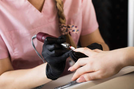 A manicurist removes gel polish from nails using a milling cutter. Hardware manicure close-up....