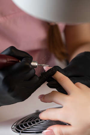 A manicurist removes gel polish from nails using a milling cutter. Hardware manicure close-up....