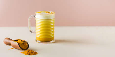 Banner with latte turmeric on a pink background. Moon milk for better sleep. Ayurvedic drink. Copy space.の写真素材