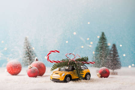 Toy car with fir branch and candy cane baubles and small Christmas trees on snow