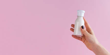 A female hand holds a plastic bottle with a cosmetic product on a pink background. Copy space.の写真素材