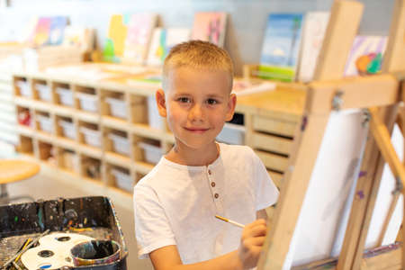 Smiling blond boy draws on canvas in the workshop. Drawing lessons for children