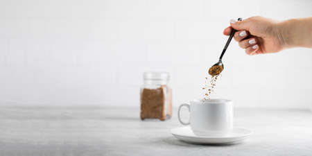 A woman adds instant coffee to a white mug on grey stone table. Copy space.の写真素材