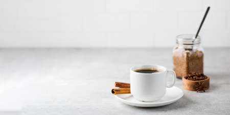 Black coffee in a white mug with cinnamon sticks on a saucer on a grey table. Copy space.の写真素材