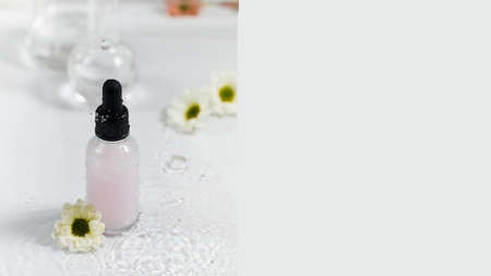 Banner bottle with skincare product and chamomile on wet surface and falling drops. Copy space.の写真素材