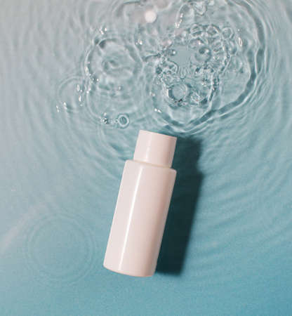 White cosmetic bottle in a blue pool with water and waves. Spa skin care.の写真素材