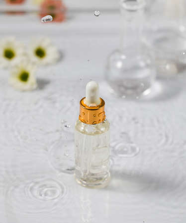 Glass dropper bottle with essential oil on wet table under falling down dropsの写真素材