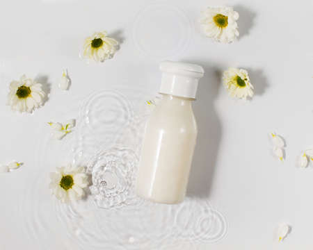 Bottles of skincare product and fresh chamomile flowers in clear splashed water