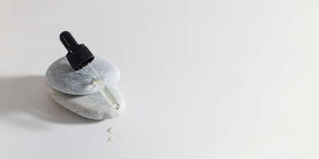 A drop of serum for the skin flows down from the pipette, which lies on the stone. Copy space.