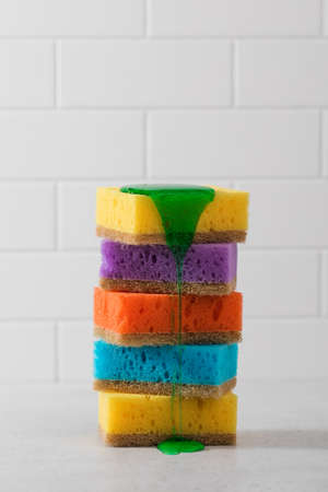 Multicolored sponges for washing dishes are stacked, green dishwashing gel flows down from above. Washing dishesの写真素材