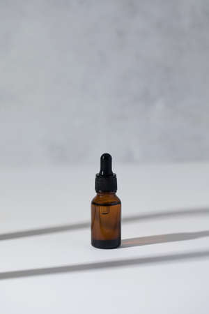 Brown glass dropper with serum for facial skin on a light grey background with shadows.. Care...