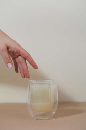 The hand reaches for a glass of healthy bone broth on a beige background.の写真素材