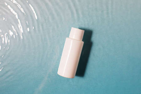 White cosmetic bottle in a blue pool with water and waves. Spa skin care.