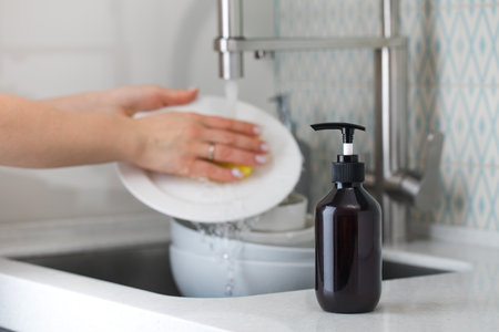 A bottle with an environmentally friendly dishwashing detergent on the background of a housewife...
