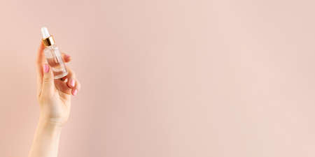 Mockup of a glass dropper with facial moisturizing oil in a female hand on a pink background. Copy space.の写真素材