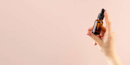 A mock-up of a brown dropper with skin oil in a womans hand. Copy space.
