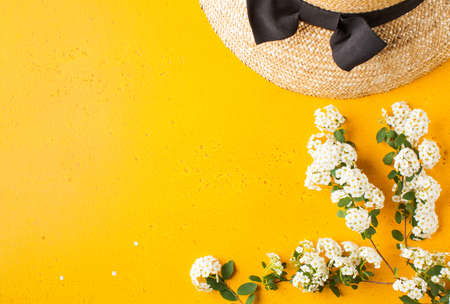 Flat lay a straw hat and a branch with white flowers on a yellow background. Summer vacation concept. Copy space.の写真素材