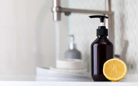 Bottle with eco friendly dishwashing detergent with lemon on the background of a sink with dirty dishes.の写真素材