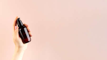 A mock-up of a brown dispenser with a natural cosmetic product in a womans hand on a pink background. Zero West.の写真素材