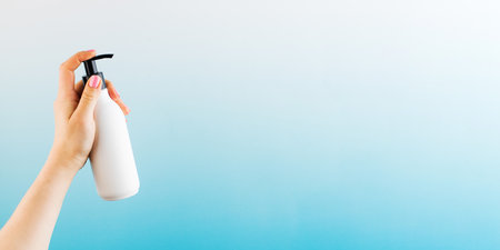 A mockup of a white dispenser with a cosmetic product in a womans hand on a blue background.の写真素材