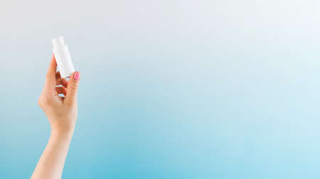 Banner a womans hand holds a white tube with a cosmetic product on a blue background. Beauty product concept. Sample.の写真素材