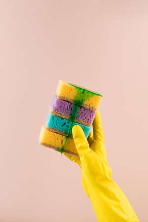 A hand in a yellow rubber glove holds colorful sponges for dishes from which green gel for washing dishes flows down.の写真素材