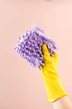 Hand in latex glove holds fluffy rag to wipe dust on beige background closeupの写真素材