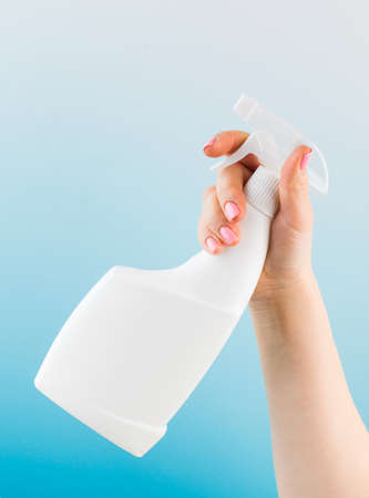 Woman hand sprays detergent from blank bottle on light blue background closeupの写真素材