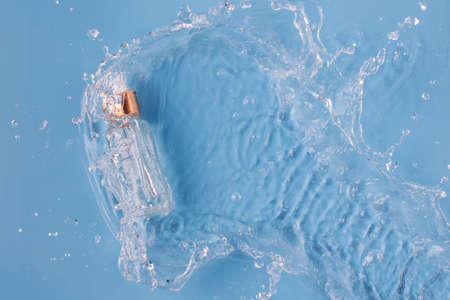 Bottle of serum falling into clean splashing water on blue background upper view