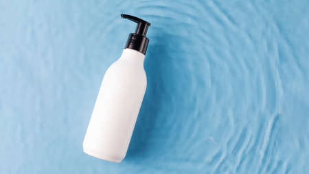 Blank dispenser bottle of cosmetics in water on blue background view from aboveの写真素材