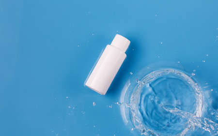 White plastic bottle with skincare product and pouring water on blue backgroundの写真素材