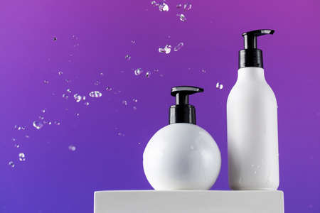 Dispenser bottles with haircare products and water drops on purple background