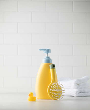 Childrens yellow dispenser with baby shampoo, comb and duck on the table. The concept of daily child...