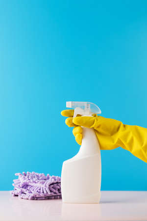 A hand in a yellow glove holds a spray bottle mockup with detergent on a blue. Cleaning, cleaning service. Copy space.の写真素材