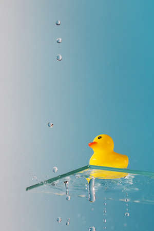 Yellow rubber duck on glass shelf and dripping water on light blue background