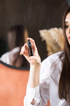 Beautiful young brunette girl with long hair holds a brown dropper with anti-aging face serum, hair oil.の写真素材